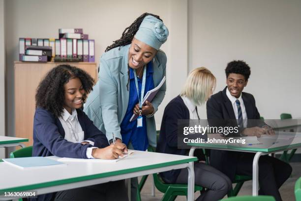 cheerful teacher helping student in secondary classroom - teachers education uniform stockfoto's en -beelden