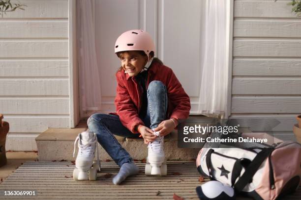 A little girl ties the laces of her roller skates on the doorstep
