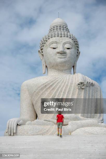 a young boy caucasian tourist ascends the steps to the giant white buddha statue in phuket, thailand - giant stone heads stock pictures, royalty-free photos & images