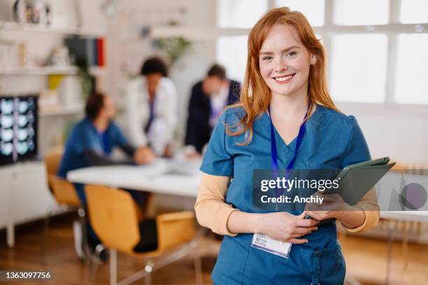 portrait of young confident happy medical professional looking at camera with medical staff brainstorming in background. - administrator stock pictures, royalty-free photos & images