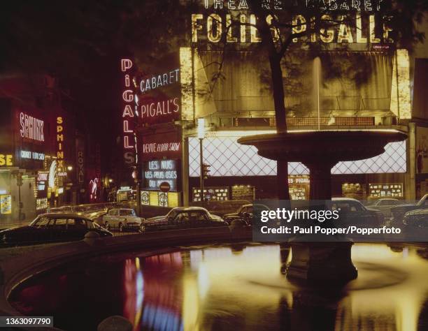 Night time view of cars parked under illuminated neon signs outside the Folies Pigalle nightclub in Place Jean Baptiste Pigalle off the Boulevard de...