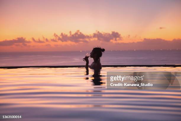 mulher asiática desfrutando vinho em uma piscina infinita ao pôr do sol - infinity pool - fotografias e filmes do acervo