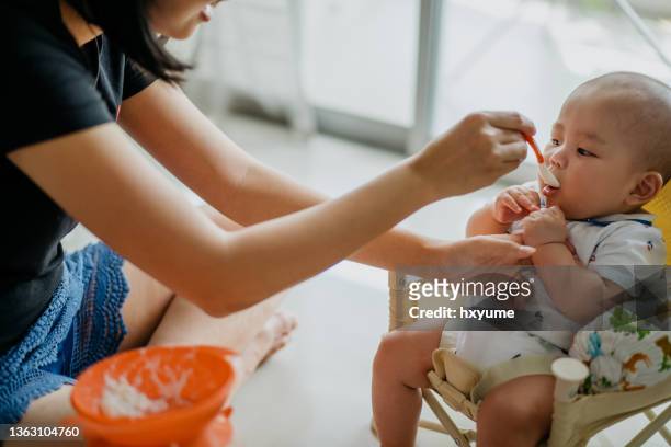 mother spoon feeding rice cereal to her baby boy - boy eating cereal stock pictures, royalty-free photos & images