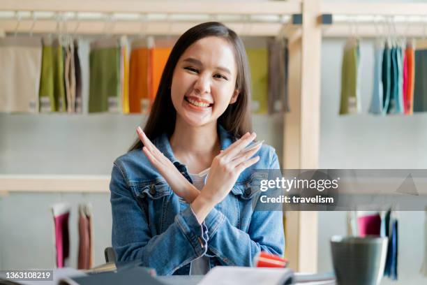 smart creative asian female hand gesture cross x together to say no hand signage,smiling asian female say no with her hand to camera at home studio background - woman hand crossed stockfoto's en -beelden