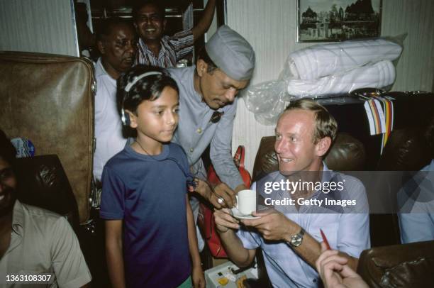 England bowler Derek Underwood accepts a cup of tea whilst a young boy listen's to a Walkman as England take the train from Bombay to Pune for the...