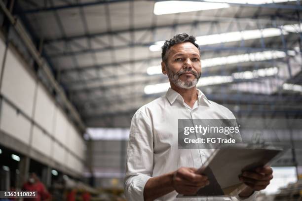homme d’affaires mature utilisant un presse-papiers dans une usine - industrial portraits character photos et images de collection