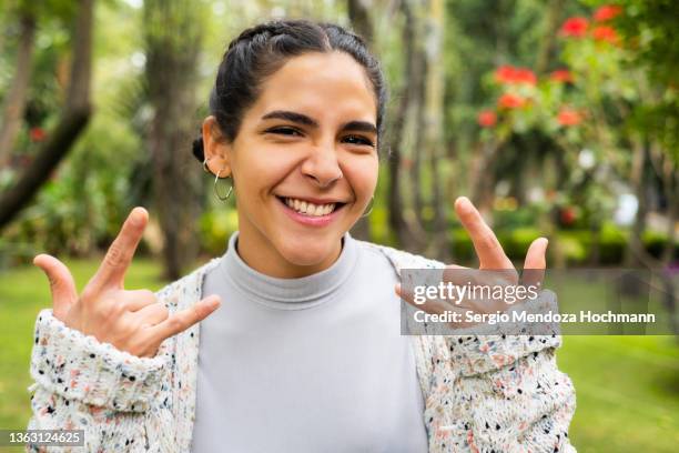 young latino woman looking at the camera and doing the heavy metal horns hand sign - horn sign stock pictures, royalty-free photos & images