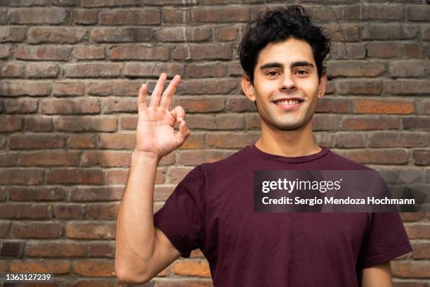 young latino man looking at the camera and giving the ok sign - guy with attitude mid shot stock-fotos und bilder