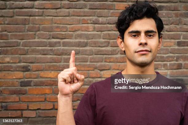 young latino man looking at the camera and giving the number one sign - guy with attitude mid shot stock-fotos und bilder