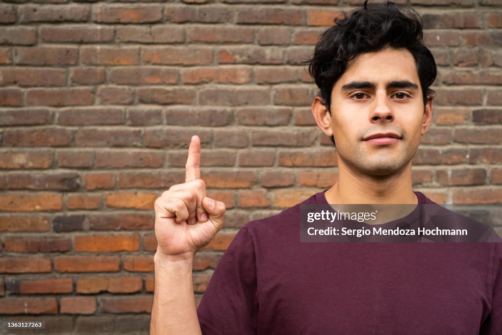 Young Latino man looking at the camera and giving the NUMBER ONE sign