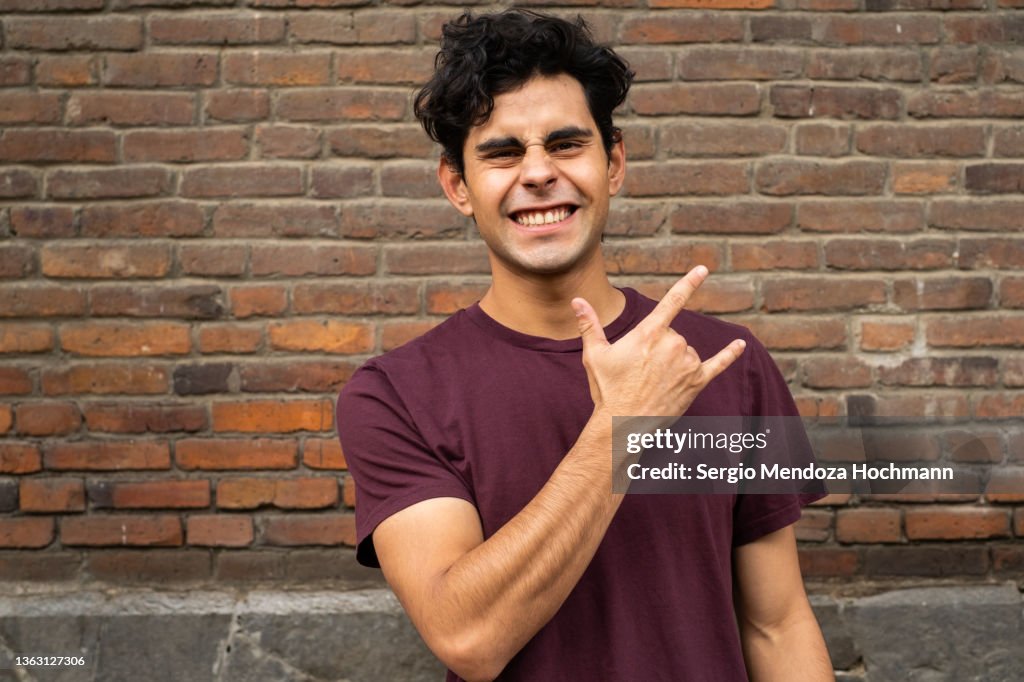 Latino man looking at the camera and doing the heavy metal horns hand sign