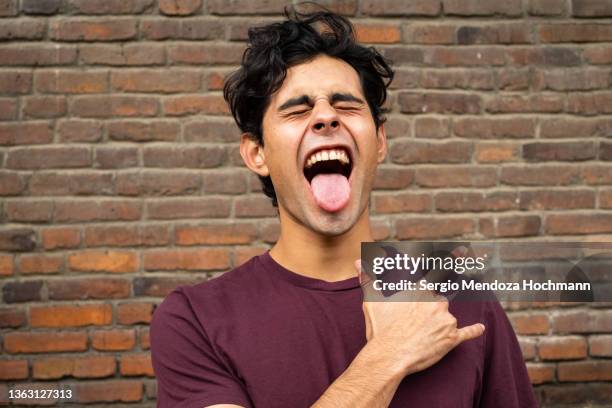 latino man with his eyes closed does the heavy metal horns hand sign while sticking out his tongue - anti bullying stockfoto's en -beelden