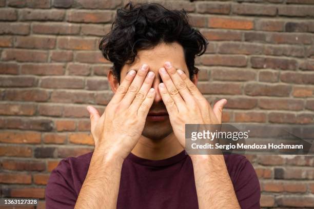 young latino man covering his eyes, see no evil - encontro entre desconhecidos imagens e fotografias de stock