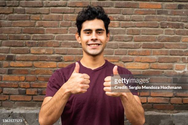 young latino man looking at the camera and giving a thumbs up - guy with attitude mid shot stock-fotos und bilder