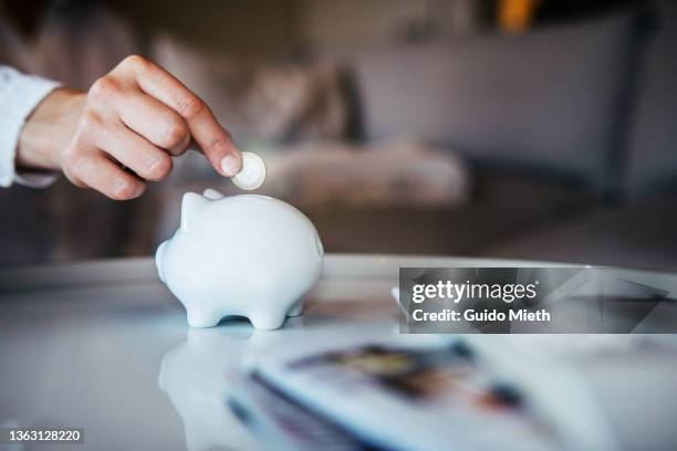 woman putting a coin in a piggy bank at home. - silver putter stock pictures, royalty-free photos & images