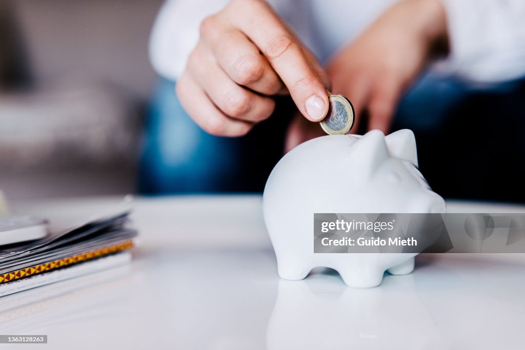 Putting a coin in a white piggy bank at home.