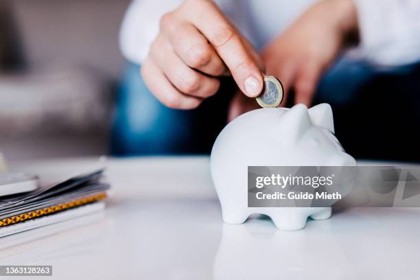 putting a coin in a white piggy bank at home. - inversion fotografías e imágenes de stock