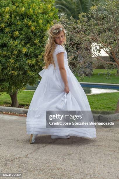 young blonde girl wearing communion dress looking back and down in beautiful garden with trees, grass and swimming pool. madrid, spain - girl white dress stock pictures, royalty-free photos & images