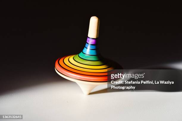 rainbow colored wooden spinning top on white surface. - spinning top stock pictures, royalty-free photos & images