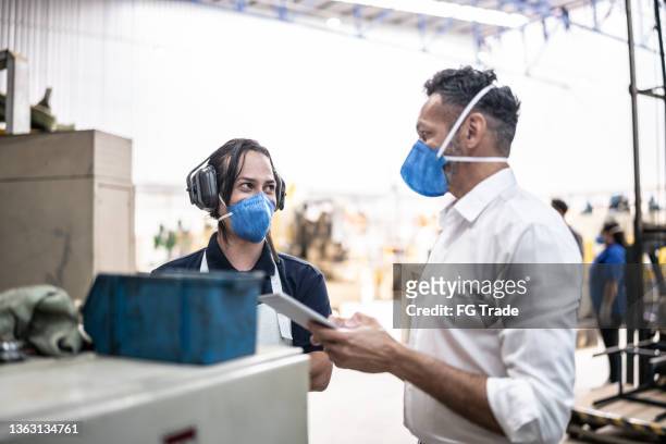 coworkers talking in a meeting at the factory/industry - using a face mask - including a non-binary person - employee engagement mask stock pictures, royalty-free photos & images