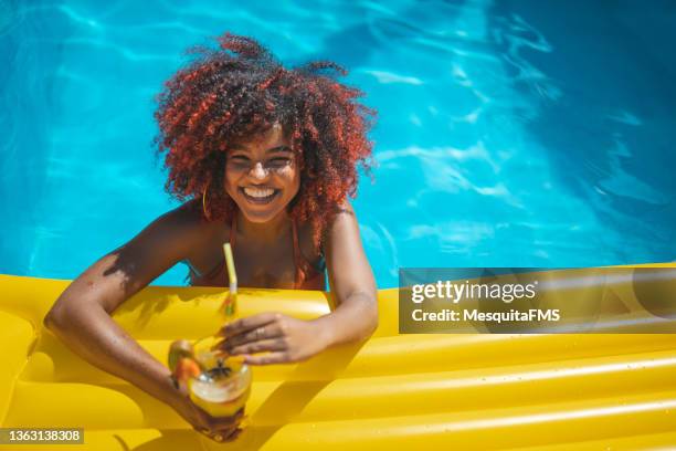 woman floating in swimming pool with tropical cocktail - cocktail and mocktail stockfoto's en -beelden