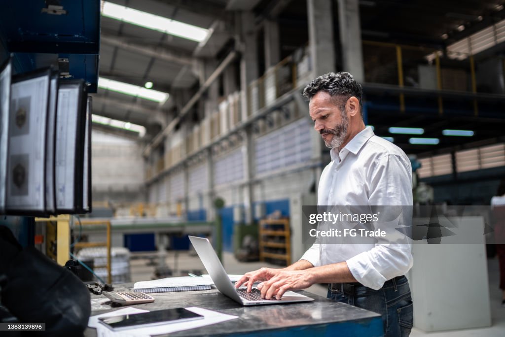 Homme d’affaires mature utilisant un ordinateur portable dans une usine
