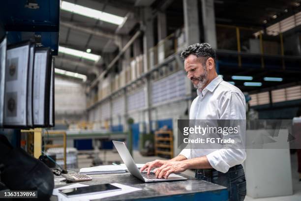 mature businessman using laptop in a factory - fabrik bildbanksfoton och bilder