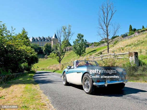 austin healey 3000 voiture de sport décapotable classique à grande vitesse avec conducteur et passager sur une route de campagne en face du château de rochechouart, haute-vienne, france - austin healey 3000 photos et images de collection