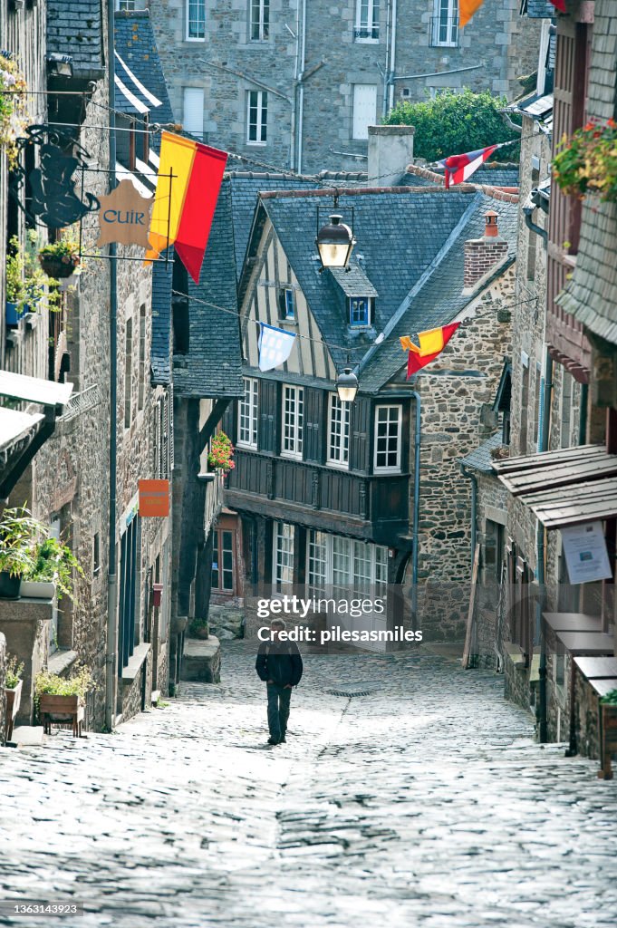 A man walks downhill between the half-timbered houses in a narrow cobbled street of the Centre Historique, Dinan, Côtes-d'Armor, France.