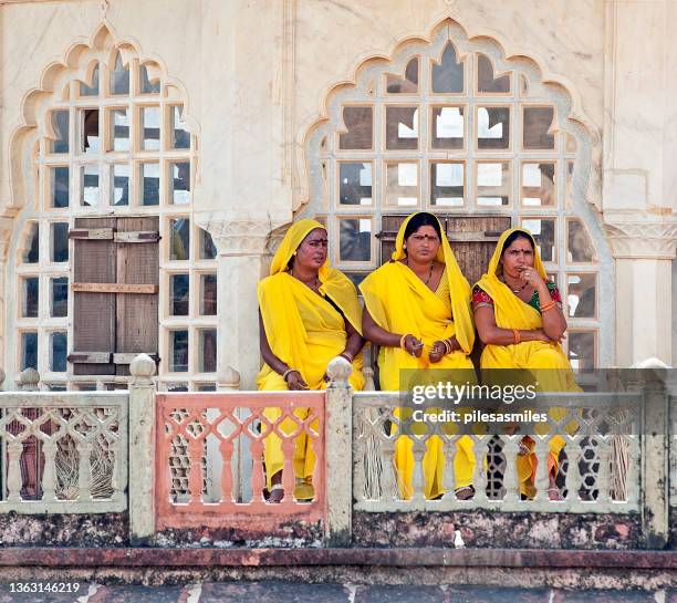 les femmes nettoyeurs du rajasthan en robe sari jaune traditionnelle font une pause devant une fenêtre ornée à amber fort, jaipur, rajasthan, inde - colors of india photos et images de collection