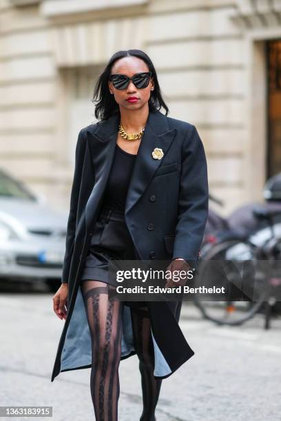 Emilie Joseph @in_fashionwetrust wears sunglasses, a long wool coat with tailored collar and golden floral brooch by Sandro Paris, Wolford suspender...