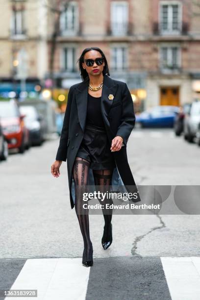 Emilie Joseph @in_fashionwetrust wears sunglasses, a long wool coat with tailored collar and golden floral brooch by Sandro Paris, Wolford suspender...