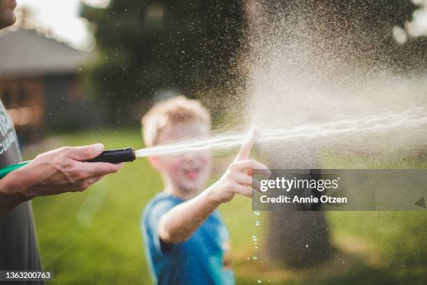 boy standing behind spray of water - wet hose ストックフォトと画像