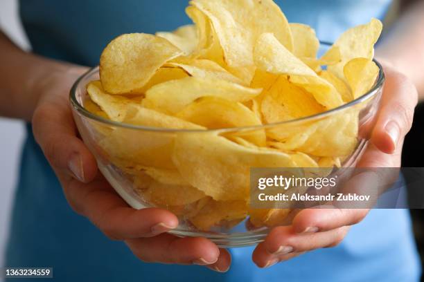 crispy fried fatty potato chips in a glass bowl or plate, on a white background or table. chips in the hands of a woman or a teenage girl, she eats them. the concept of an unhealthy diet and lifestyle, the accumulation of excess weight. - chip stock-fotos und bilder