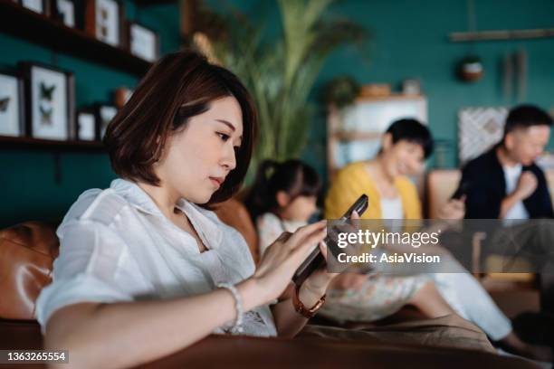 multi-generation asian family relaxing in the living room at home and using various wireless technology. focusing on young woman in foreground. technology use across all age groups - hong kong grandmother stock pictures, royalty-free photos & images