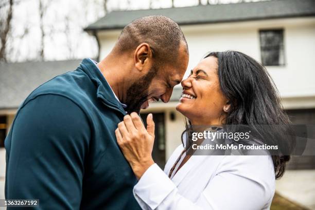 married couple embracing in front of residential home - couple laughing hugging stock pictures, royalty-free photos & images