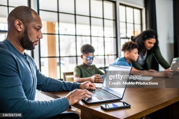 father working from home in residential kitchen with family in background - indian family in their 40's with kids imagens e fotografias de stock