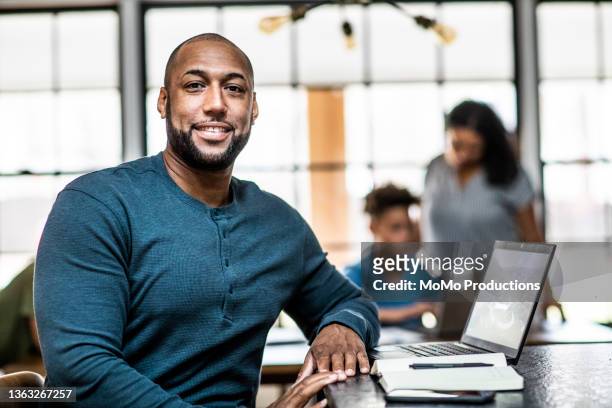 portrait of father working from home in residential kitchen with family in background - minority groups professional stock pictures, royalty-free photos & images