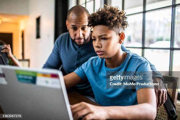 father helping teenage son with homework in residential kitchen - college homework stock pictures, royalty-free photos & images