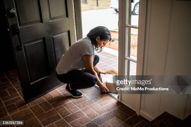 woman picking up delivery package in residential doorway - entregar fotografías e imágenes de stock