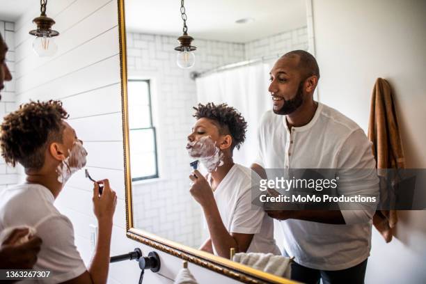 father teaching teenage son to shave in bathroom - lifestyle moments stockfoto's en -beelden