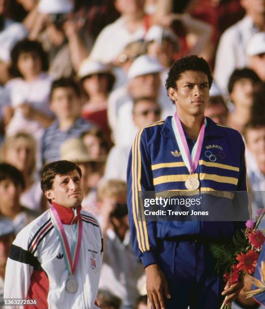 Gold medallist Joaquim Cruz from Brazil and second placed silver medallist Sebastian Coe of Great Britain stand on the podium for the playing of the...