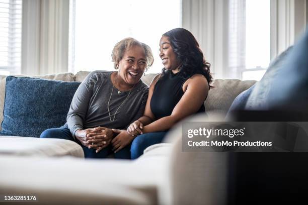 senior mother talking with adult daughter on sofa - lifestyle moments stockfoto's en -beelden