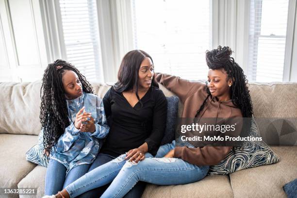 mother talking with teenage daughters on sofa - girl in black jeans stockfoto's en -beelden
