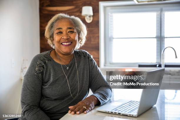 portrait of senior woman working using laptop in residential kitchen - name tag stock-fotos und bilder