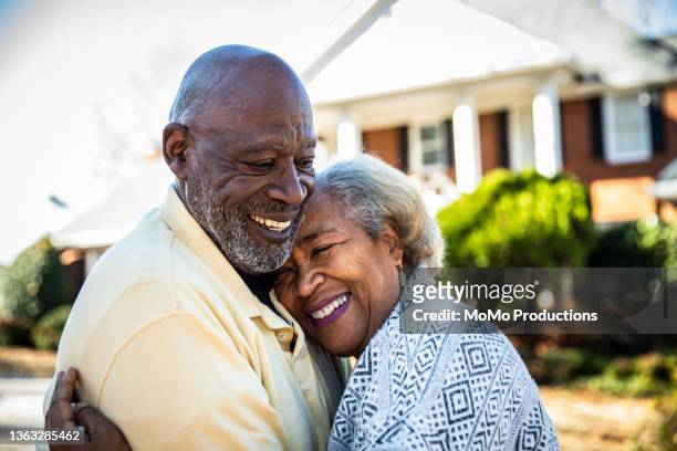 senior couple embracing in front of residential home - man hugging woman foto e immagini stock