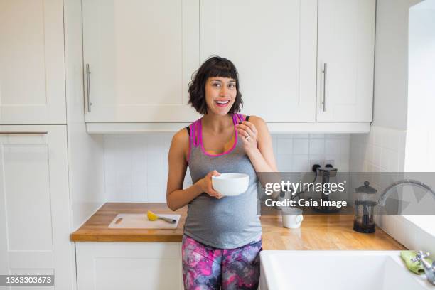 portrait happy pregnant woman eating in kitchen - filipino family eating fotografías e imágenes de stock