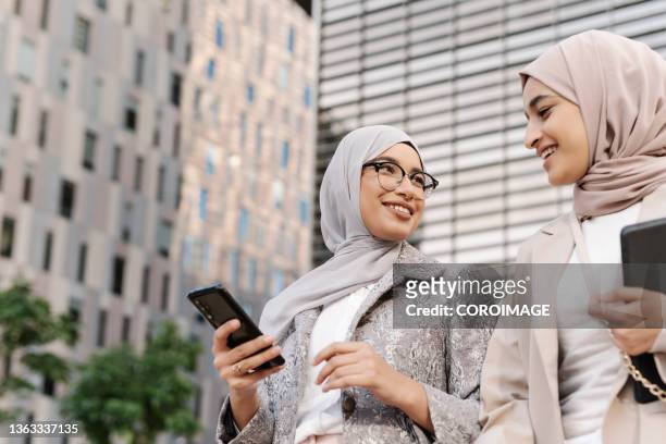 two muslim businesswomen walking together outdoors on the street during a break from work. - religiöse kleidung stock-fotos und bilder