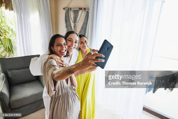 medium wide shot of smiling bridesmaid taking selfie with bride and mother in luxury suite before wedding - luxury hotel room stock pictures, royalty-free photos & images