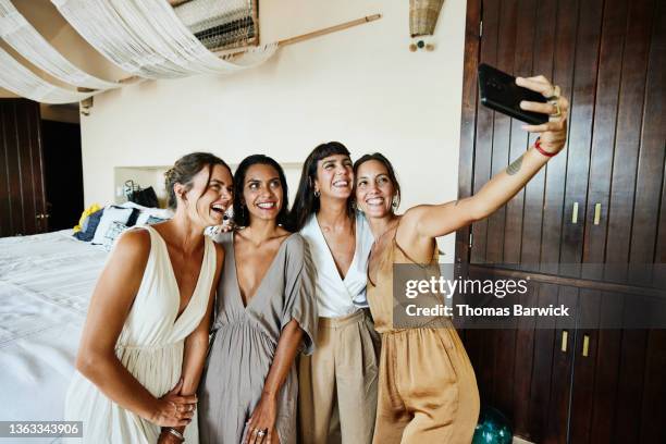 medium wide shot of smiling and laughing bridesmaids taking selfie in luxury hotel suite before wedding - luxury woman stock-fotos und bilder